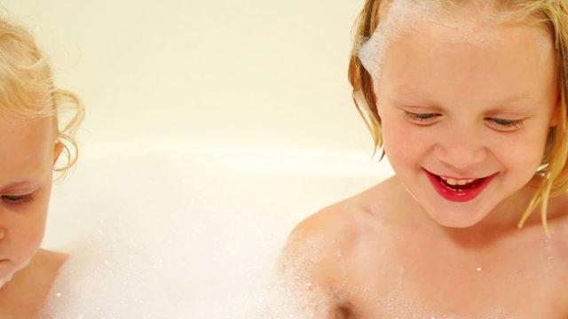 A baby and a little girl play in the suds while taking a bubble bath