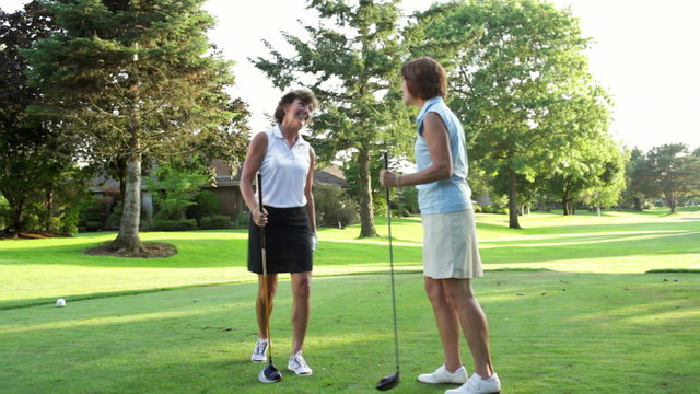 Two female golfers on a tee box greet each other. Wide shot.