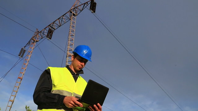 Power line engineer inspecting power lines and inputting and analyzing data in his laptop
