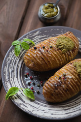 Close-up of baked hasselback potato with spices and basil pesto