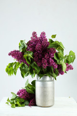 Purple lilac flowers in watering can on white wooden background