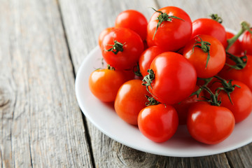 Fresh cherry tomatoes in plate on grey wooden background