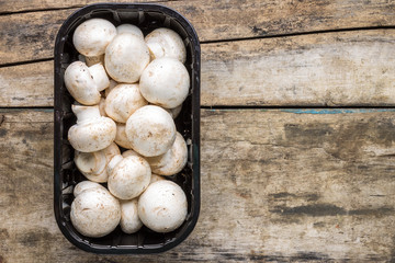 Fresh raw mushrooms in plastic container on wooden background