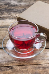 Cup of red karkade tea with book on wood background