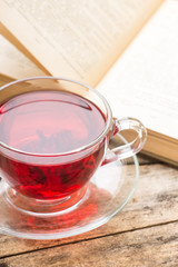 Glass cup of Karkade tea with old opened book at the table