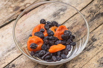 Dried fruits in glass bowl on wooden background.