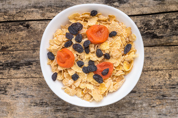 Corn flakes with dried fruits on wood background