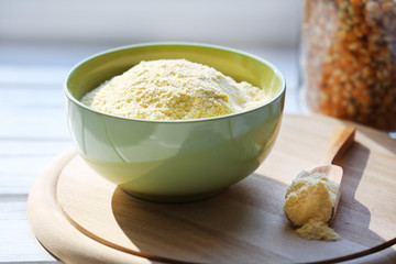 Flour in bowl with scoop on cutting board near glass bottle of corn on wooden planks background