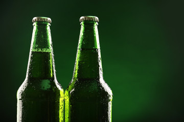 Glass bottles of beer on dark green background