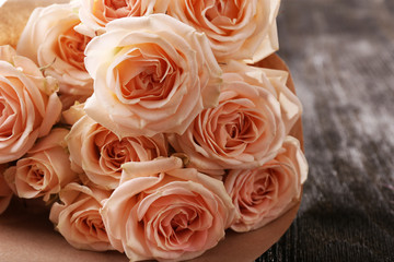 Bouquet of beautiful fresh roses wrapped in paper on wooden table, closeup