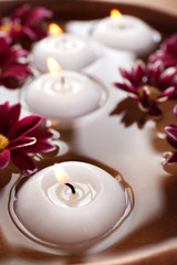 Bowl of spa water with flowers and candles, closeup