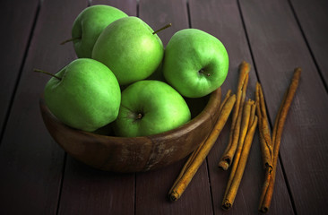 Green apples with cinnamon sticks on wooden background