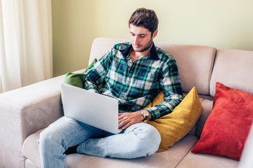 Handsome young man sitting on couch working on his laptop