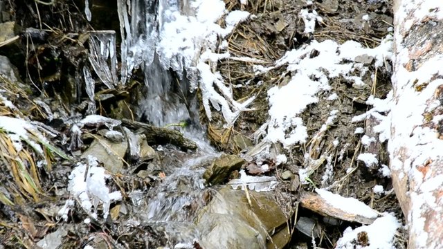 Mountain brook flows on stony snowy soil with icicles and ice