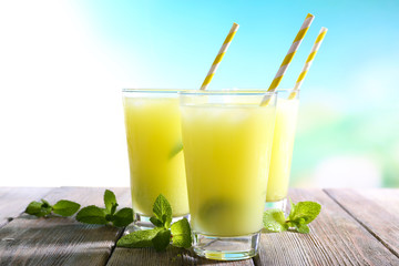 Glasses of cocktails on wooden table on bright blurred background
