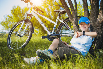 happy kid with a bicycle resting under a tree