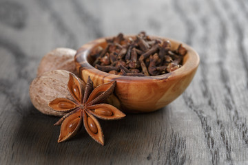 anise stars cloves and nutmeg in olive bowl on oak table, rustic