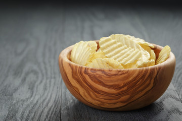 rippled organic chips in wood bowl on wooden table with copy