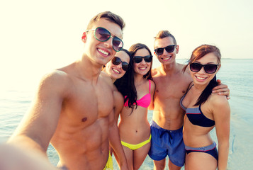 group of smiling friends making selfie on beach