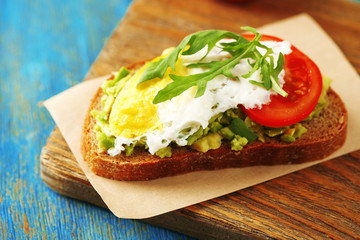 Tasty sandwich with egg, avocado and vegetables on cutting board, on color wooden background