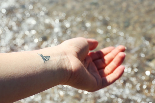 Close up of hand of young woman with ship tattooed in it, on sea background
