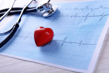 Cardiogram with stethoscope and red heart on table, closeup