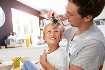 Fototapeta premium Father Brushing Son's Hair At Breakfast Table