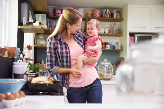 Mother Cooking Meal Whilst Holding Daughter In Kitchen