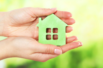 Female hands holding model of house on bright background