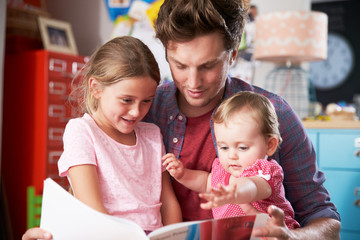 Father Reading Book With Daughters In Bedroom