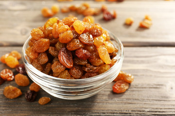 Raisins in glass saucer on wooden table, closeup