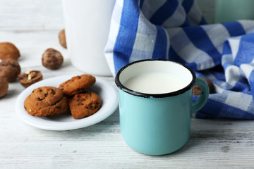 Milk in mug with walnuts and cookies on wooden background