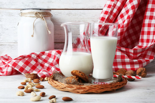 Milk in glassware with walnuts and cookies on wooden table with napkin, closeup