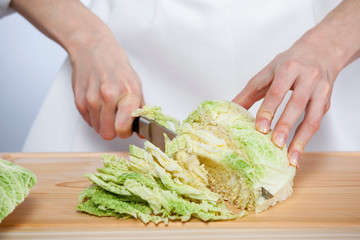 Female hands chopping savoy cabbage on wooden board