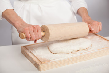 Unrecognizable cook's hands rolling out dough on wooden board, gray background