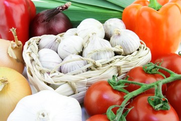Small solo garlic bulbs in a woven basket with vegetables around it.