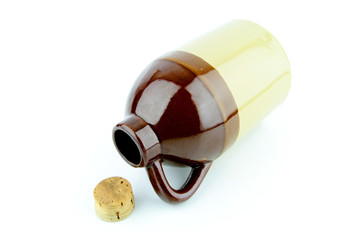 Old clay jug with a cork used to hold booze, with a filled glass next to it.