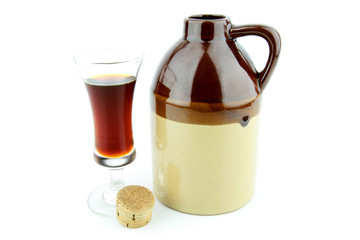 Old clay jug with a cork used to hold booze, with a filled glass next to it.