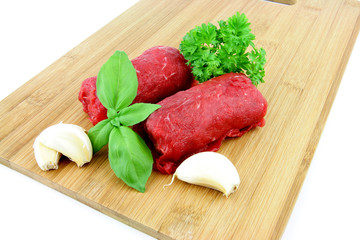 Dutch meat roll called "Blinde vink" made of veal ground beef with a thin cutlet of veal on the outside, on a cutting board with some herbs.
