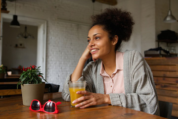 Smiling young woman sitting at home with glass of orange juice