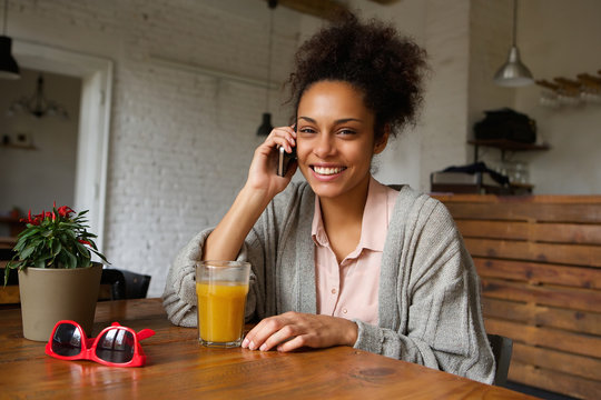 Smiling young woman sitting at home talking on mobile phone