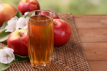 Glass of apple juice and apples on wooden table