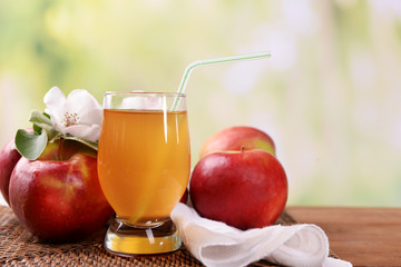 Glass of apple juice and apples on wooden table, on nature background