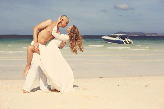 Beautiful young love couple kissing and dancing on the beach near blue tropic sea