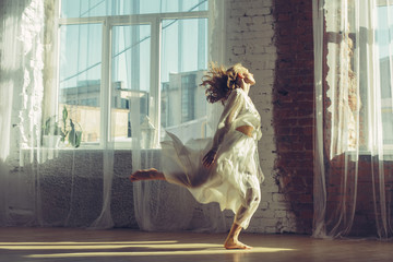 Beautiful woman in light interior with big windows listening music and dancing. Home comfort concept