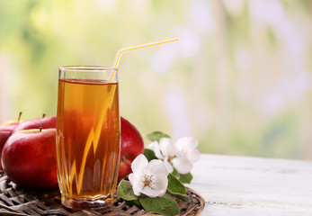 Glass of apple juice and apples on wooden table, on nature background