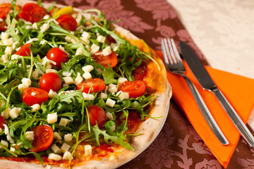 Pizza with rucola and cherry tomatoes on a teble of italian rest