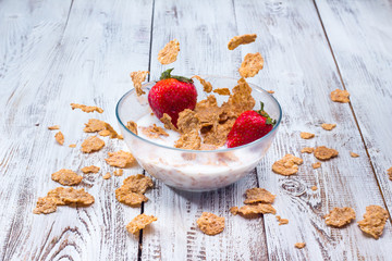 Milk, cereal and strawberries on a wooden table.