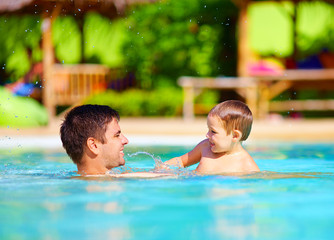 joyful father and son having fun in pool, summer holidays