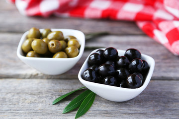 Green and black olives in bowl on grey wooden background